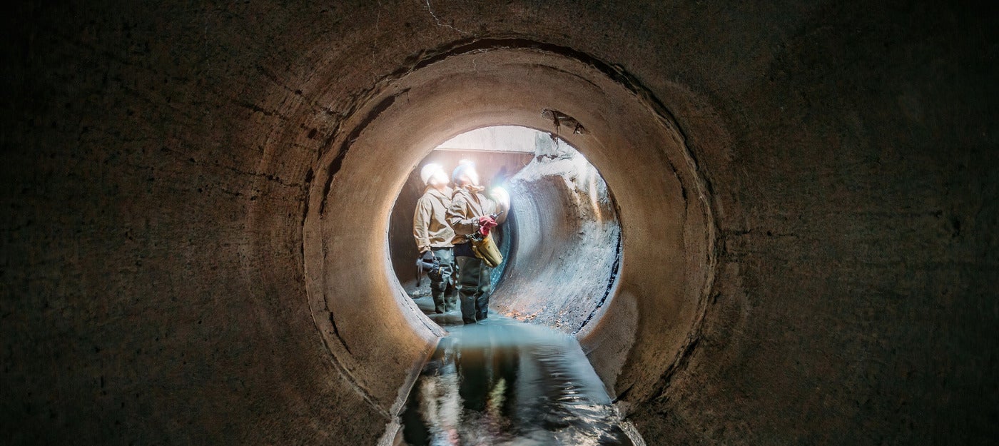 Two workers in sewer wearing safety gear and cap lights